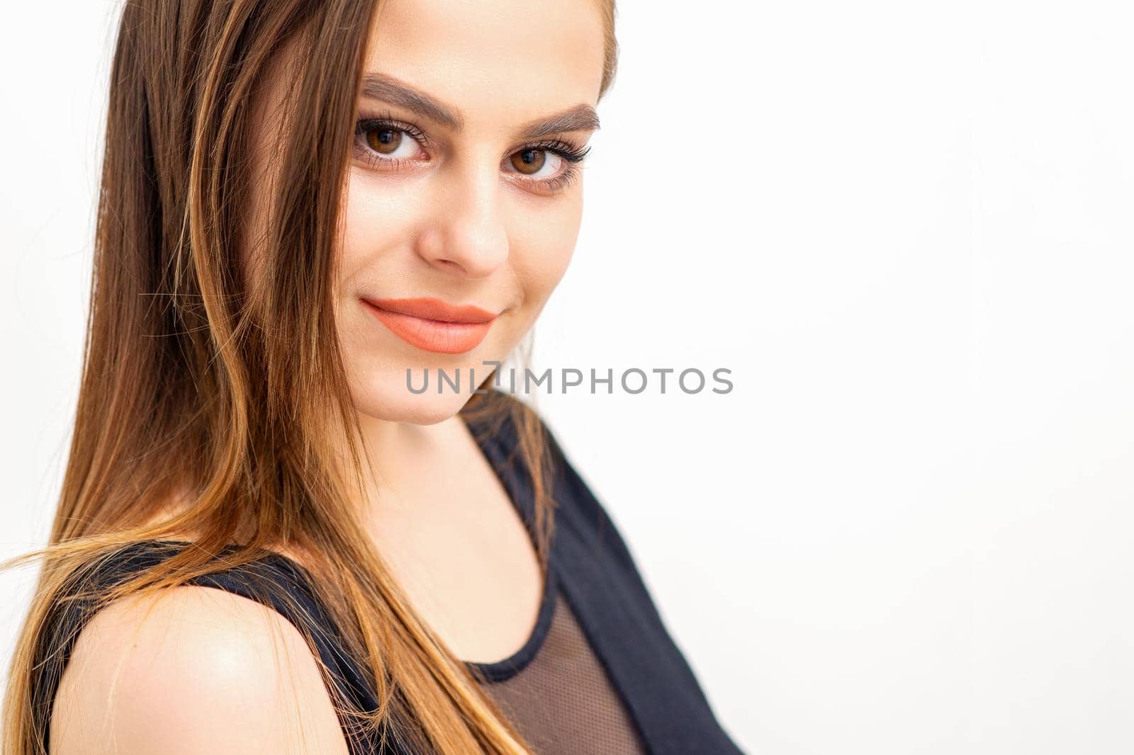 Portrait of a beautiful young caucasian smiling brunette woman with long straight hair standing and looking at the camera on white background