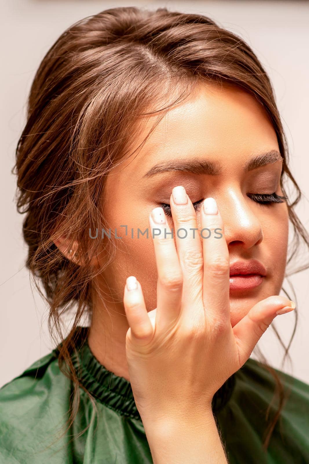 The hand of a makeup artist applies eye shadow on the eyelid of a young Caucasian woman with fingers in a beauty salon