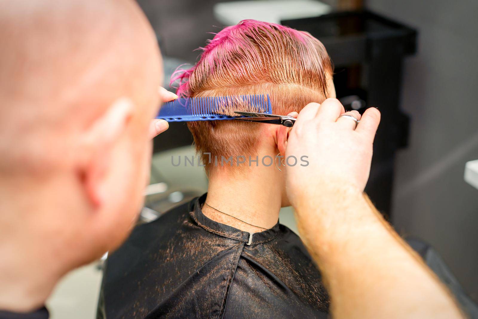 Haircut of dyed short pink wet hair of young caucasian woman by a male hairdresser in a barbershop. by okskukuruza