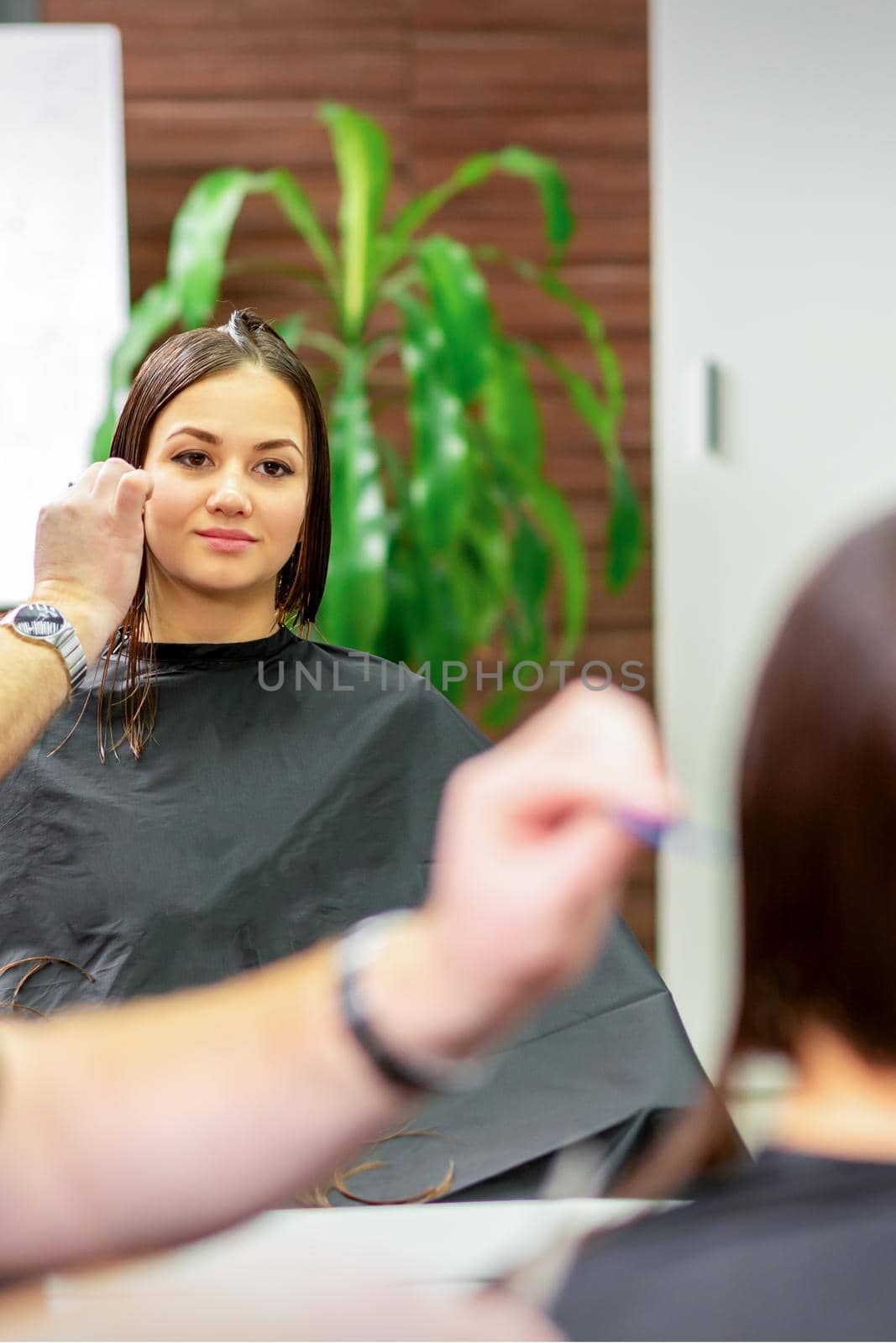 Reflection in the mirror of the young caucasian woman sitting and receiving haircut by male hairdresser at hairdresser salon