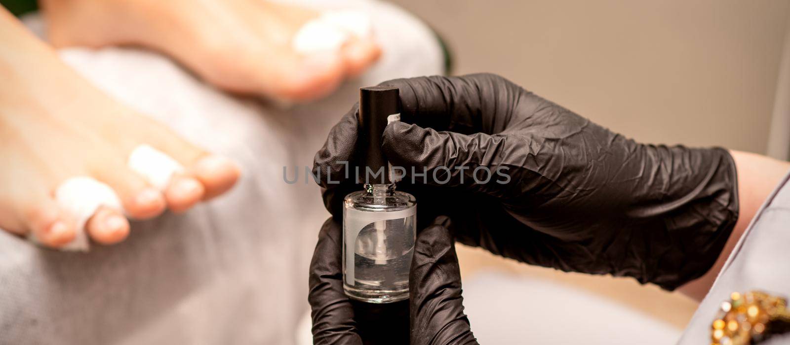 Transparent nail polish in the hands of a manicure master while painting nails on a female feet