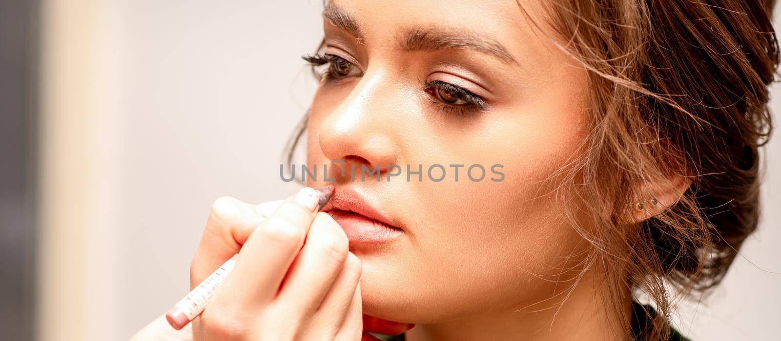 Lips makeup. Makeup artist applies contour with a pencil to the lips of a young woman in a beauty salon