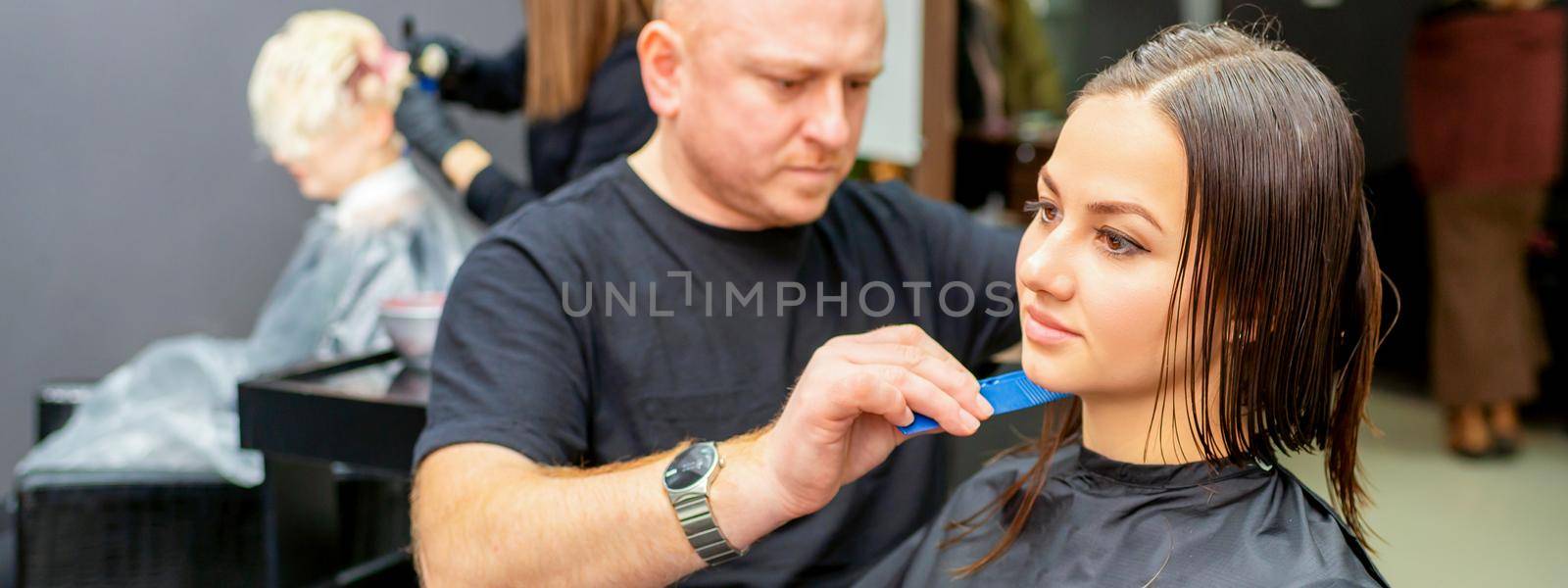 Haircut of long wet hair of young caucasian woman by a male hairdresser in a hairdresser salon. by okskukuruza