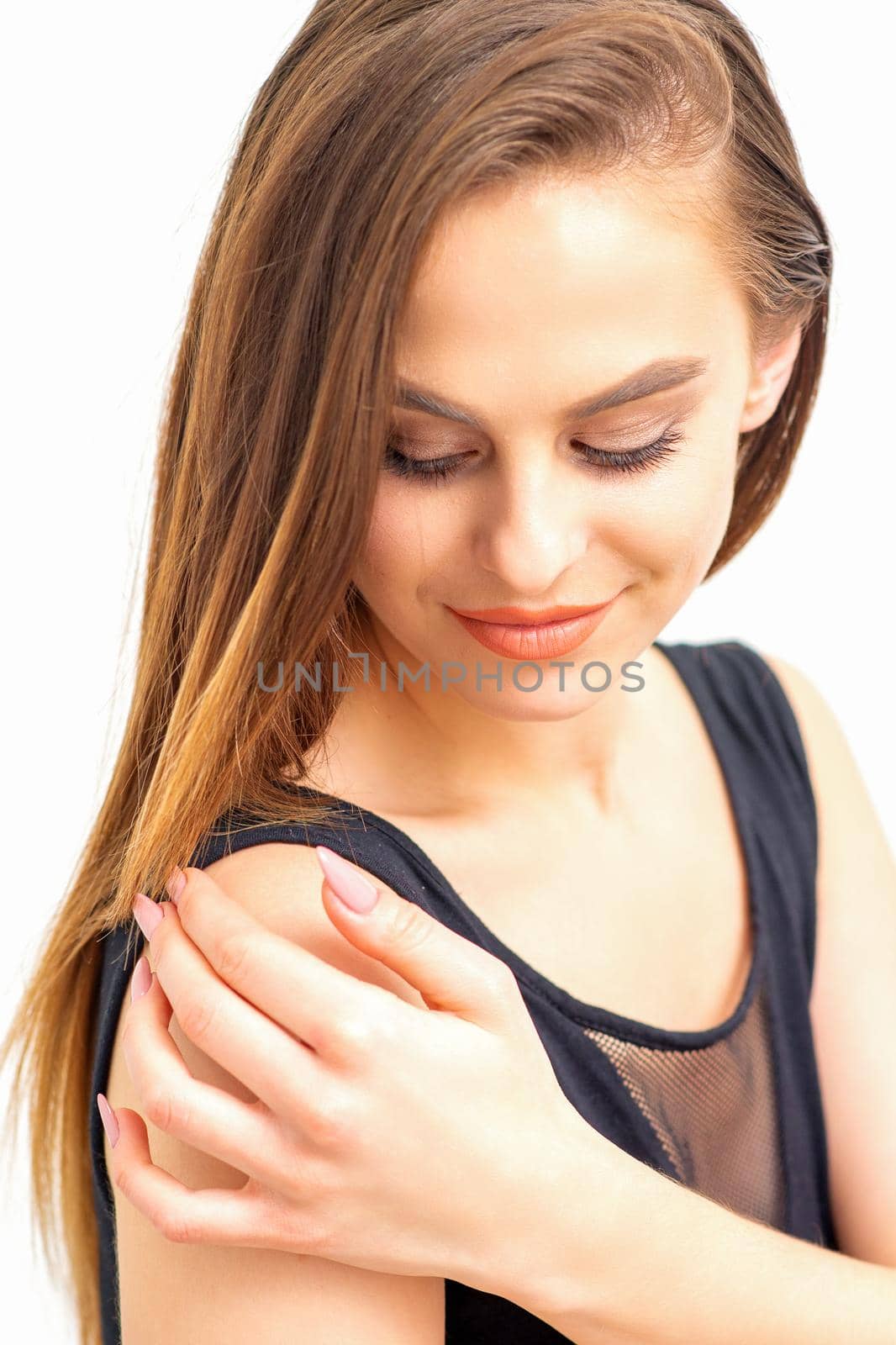 Portrait of a beautiful young caucasian smiling brunette woman with long straight hair standing and looking down on white background