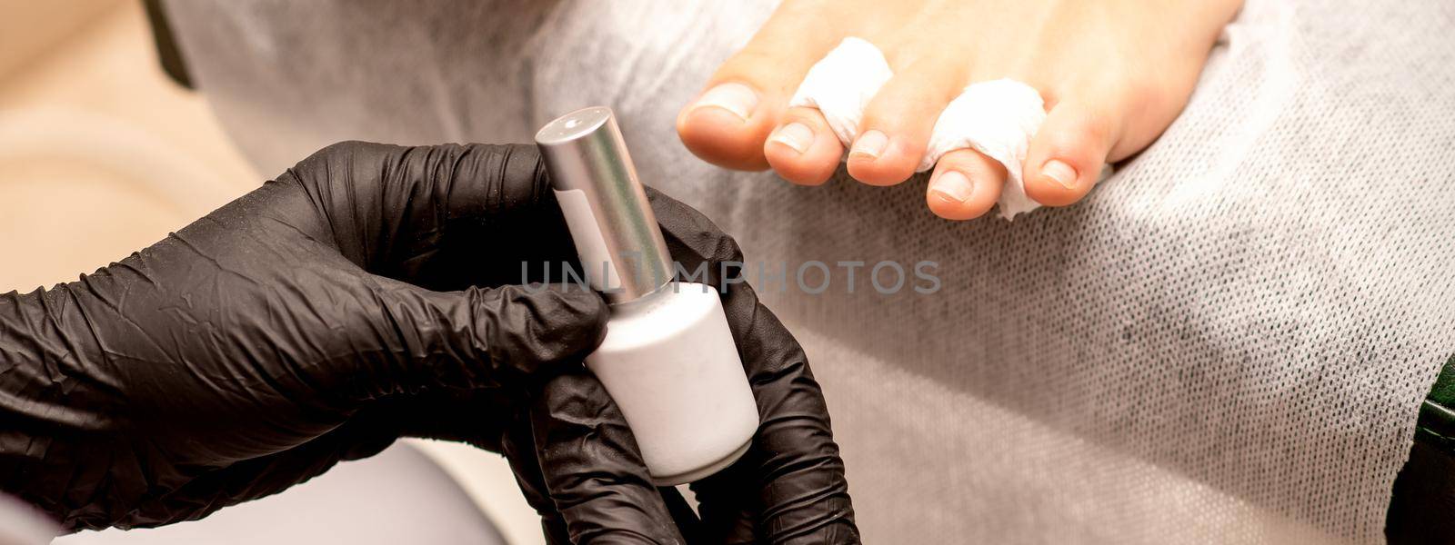 White nail polish in the hands of a manicurist while painting nails on a female feet, closeup. by okskukuruza