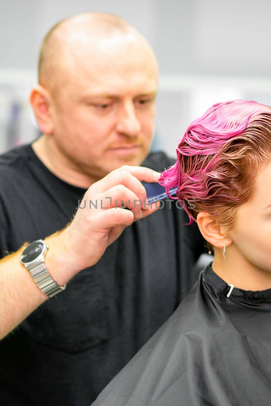 Haircut of dyed short pink wet hair of young caucasian woman by a male hairdresser in a barbershop. by okskukuruza