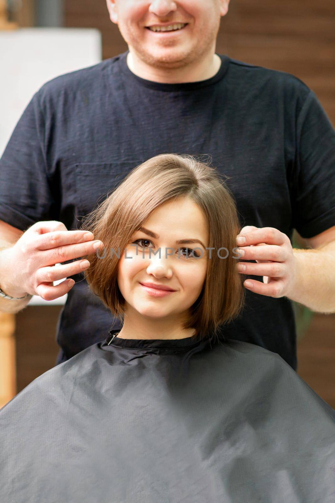 Gorgeous brunette short hair woman and her male hairdresser looking and checking out hairstyle. Beautiful hairstyle of a young brunette woman, results of hair treatment in a beauty salon