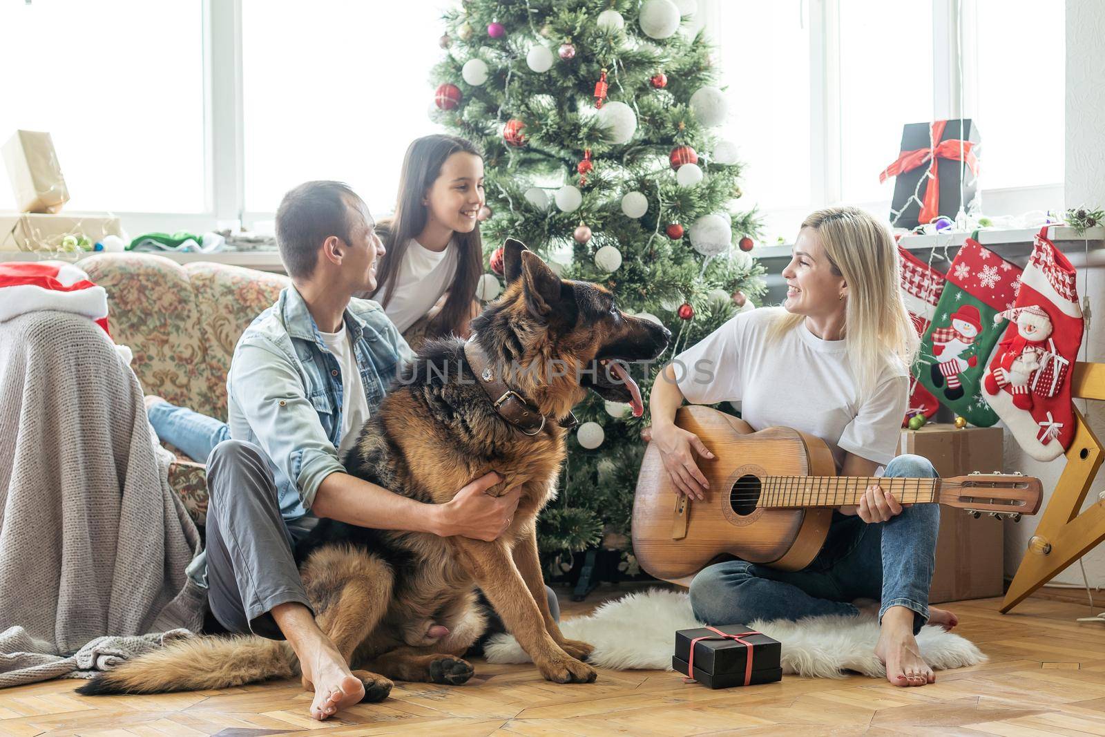 Excited girl and her family sitting on the floor near christmas tree and smiling. family during Christmastime.