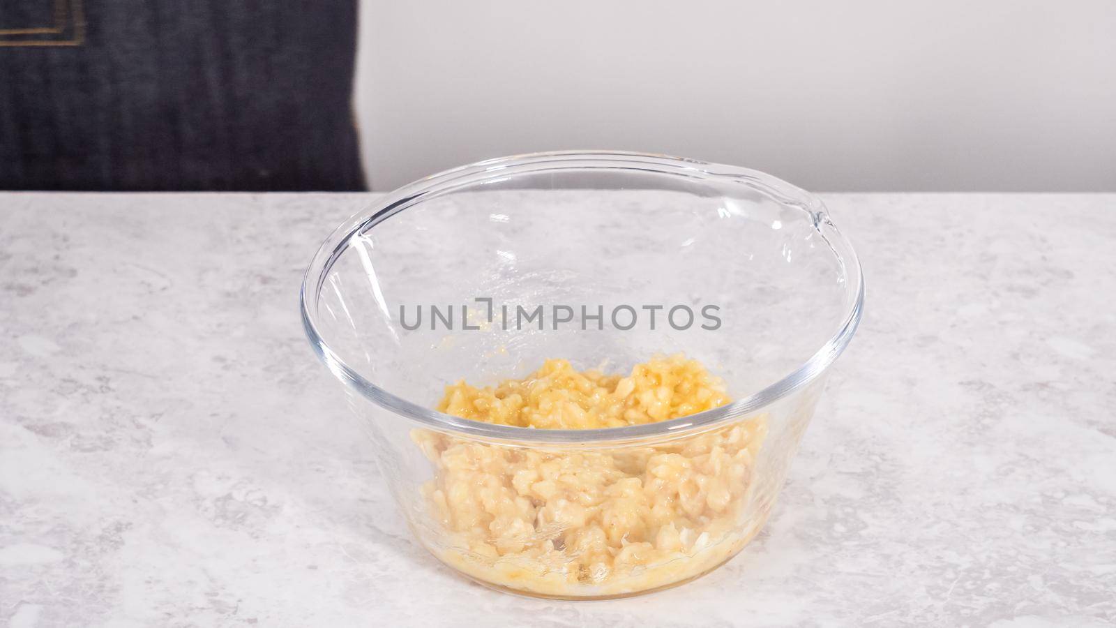 Step by step. Smashing riped bananas in a glass mixing bowl to prepare coconut banana pancakes.