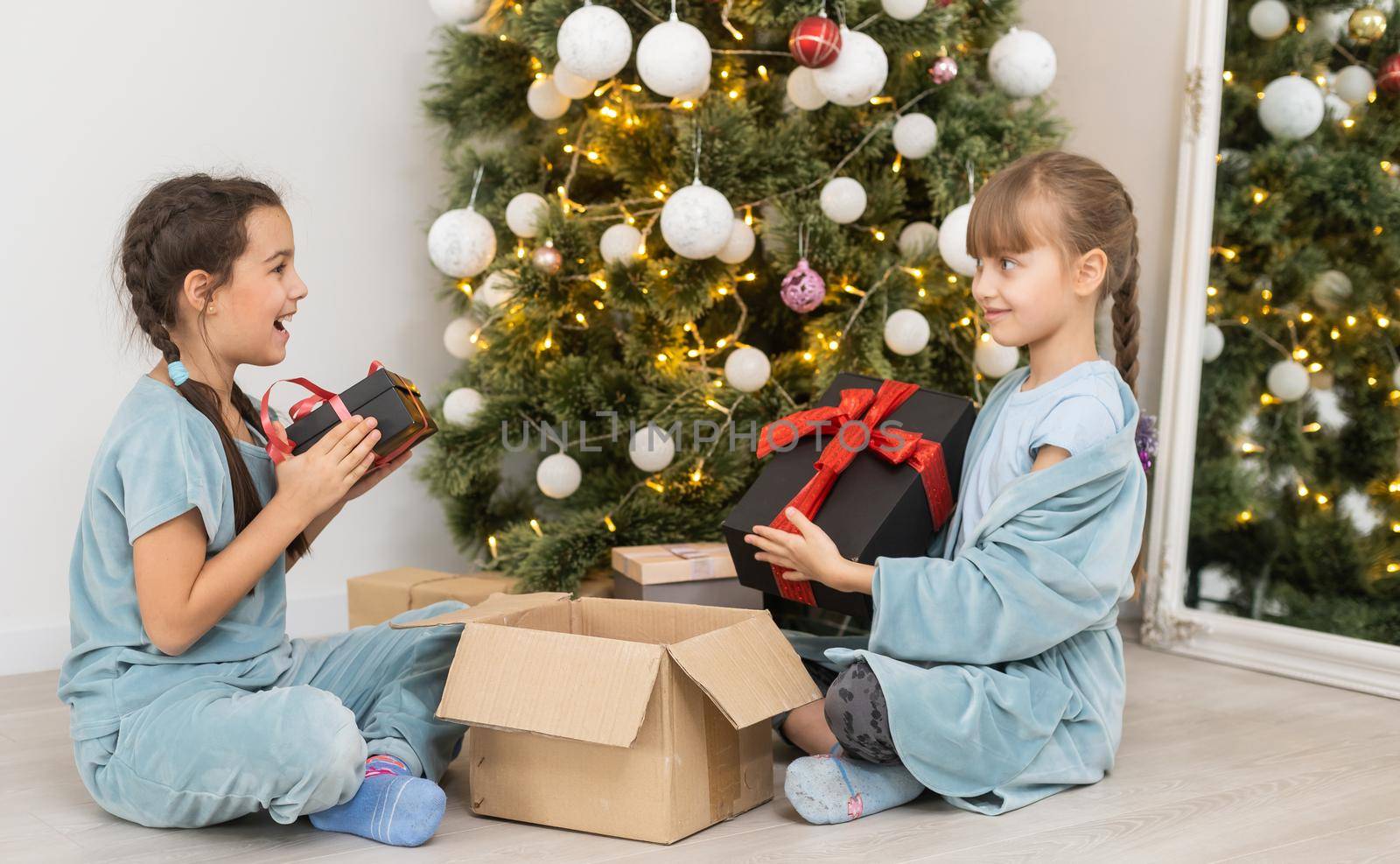 Two little girls open Christmas present under the Christmas tree.