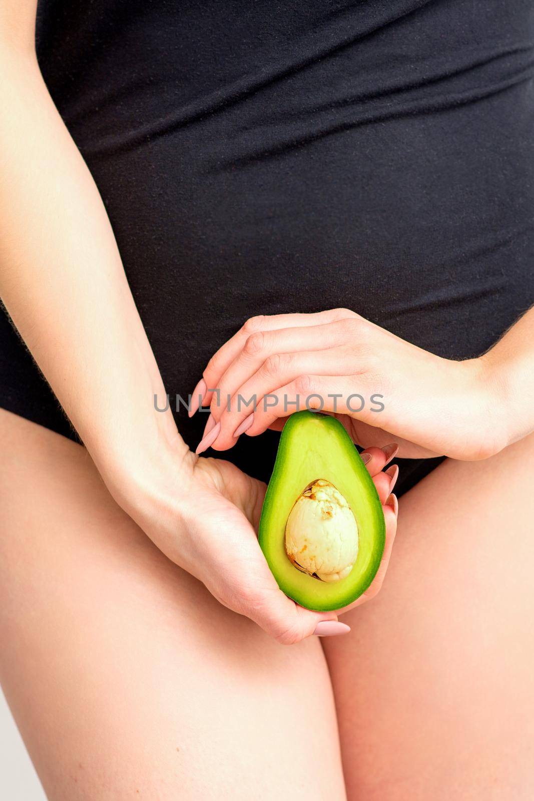 Healthy nutrition and pregnancy concept. Young woman holding one half of an avocado fruit close to her belly over a white background