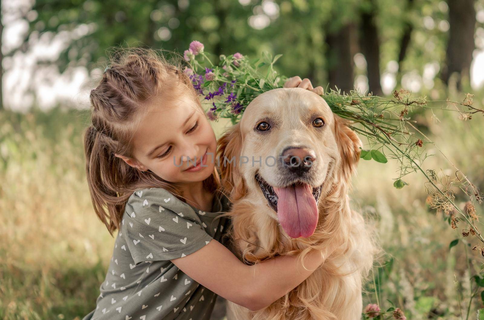 Portrait of beautiful preteen girl petting and hugging golden retriever dog looking at the camera outdoors. Kid with doggy pet in the field in summer time