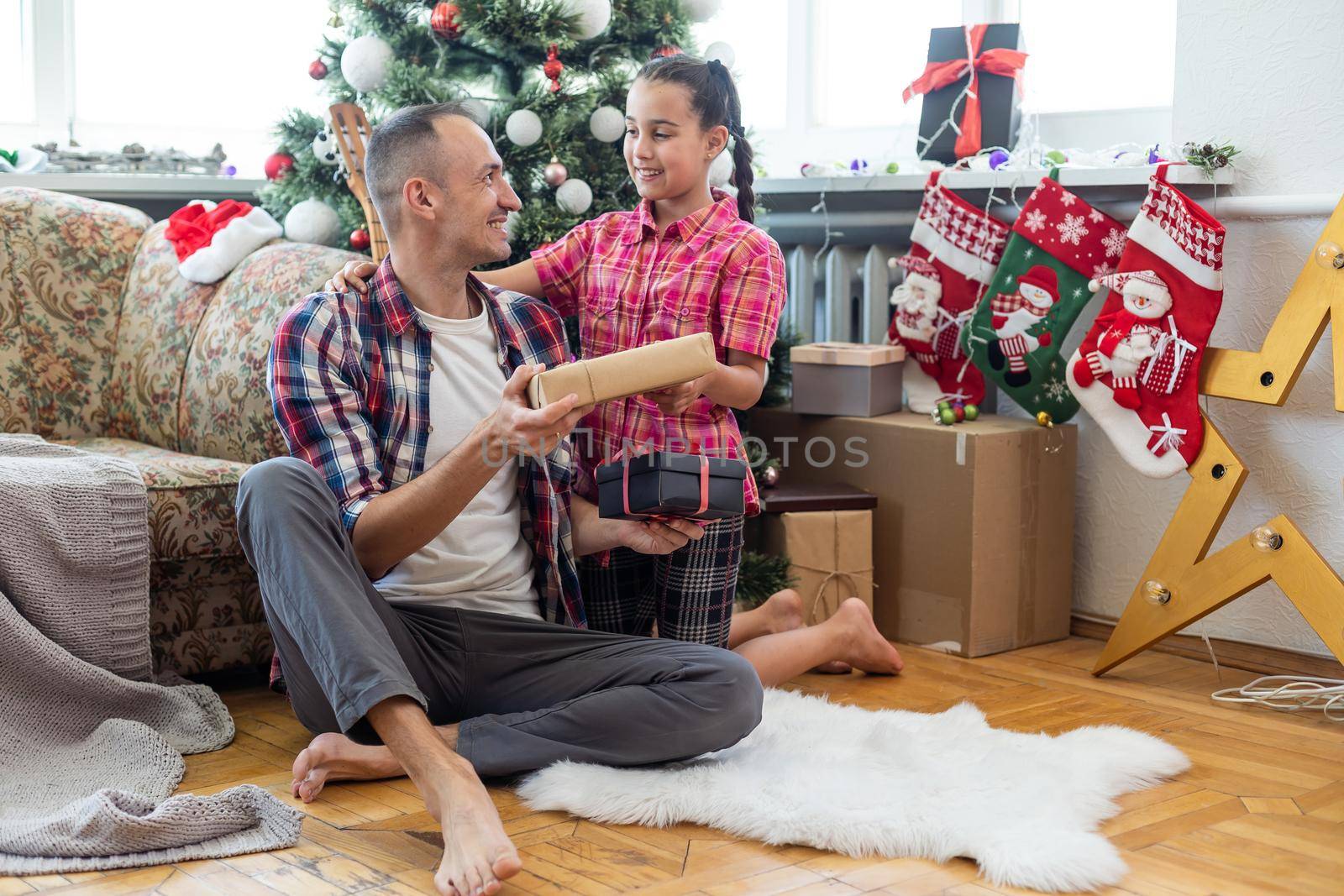 Little four year girl with her dad in living room decorated by Christmas tree and present gift box, the light give cozy atmosphere. New Year and merry xmas daughter and father concept