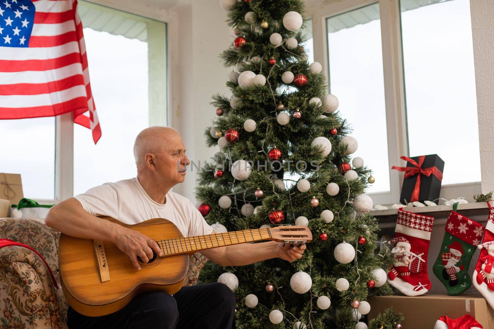 man holding guitar in front American Flag haning behind him at christmas.