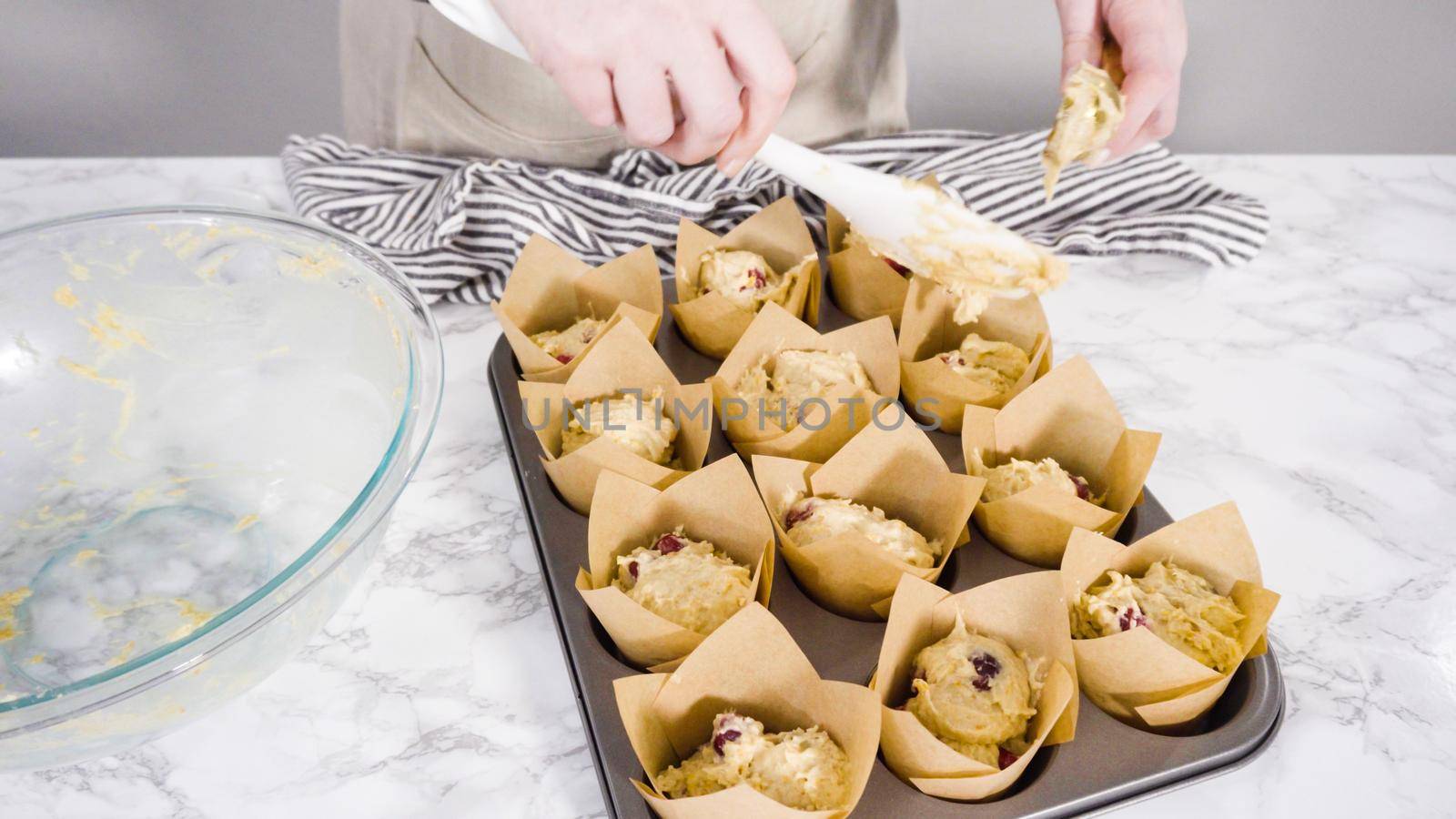 Step by step. Scooping dough into tulip muffin liners with mixture scoop to bake cranberry muffins.