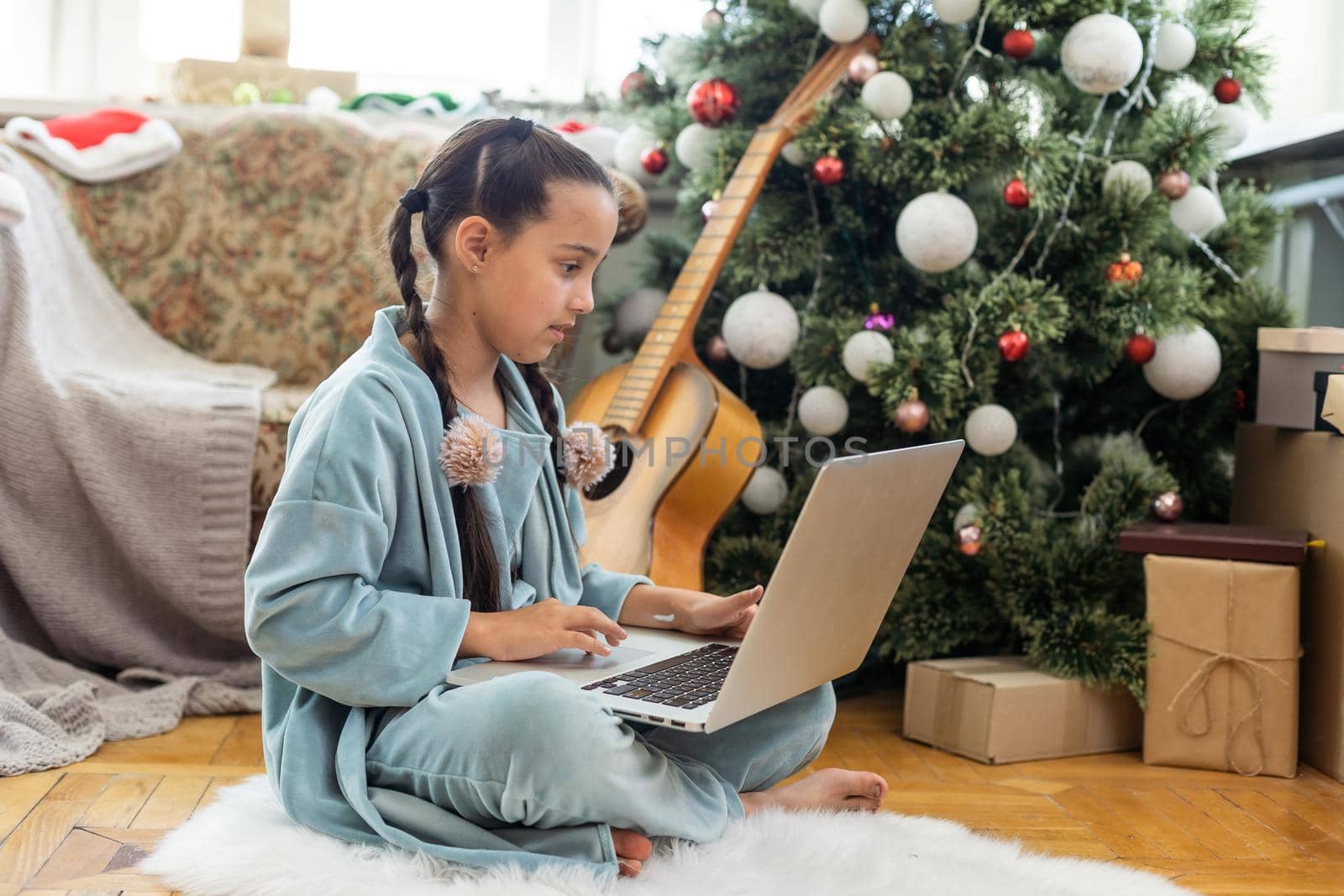 little girl sitting, looking at a laptop with a smile before Christmas.