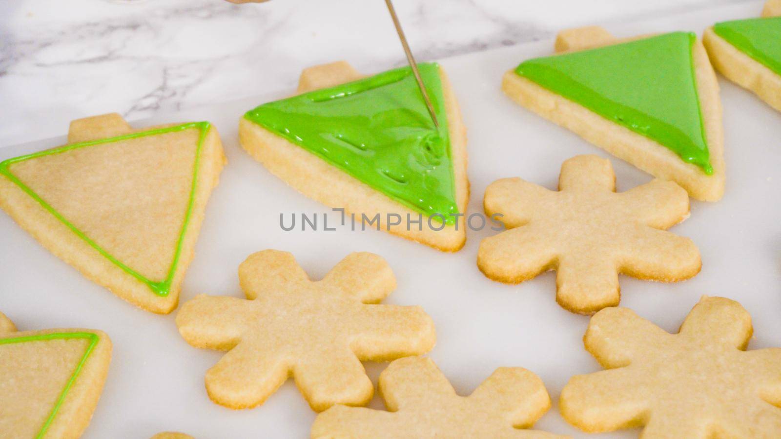 Stp by step. Icing Christmas tree-shaped sugar cookies with green royal icing.