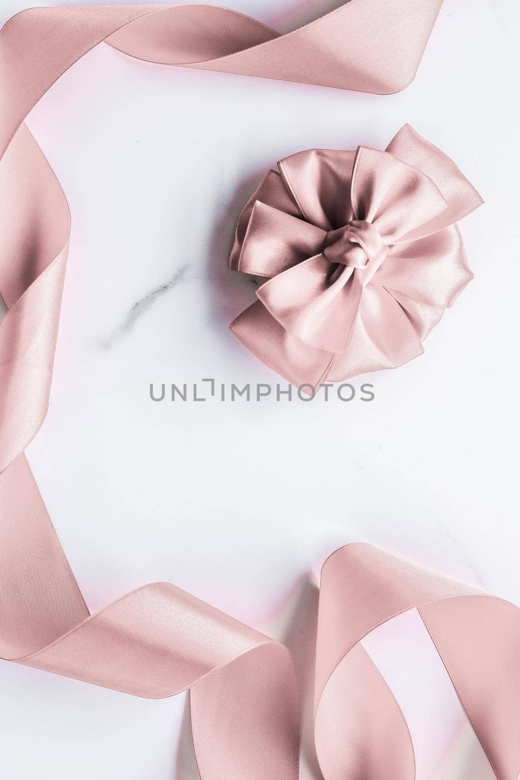 Birthday, wedding and girly branding concept - Beige silk ribbon and bow on marble background, glamour present mockup and fashion gift decoration for luxury beauty brand holiday flatlay design