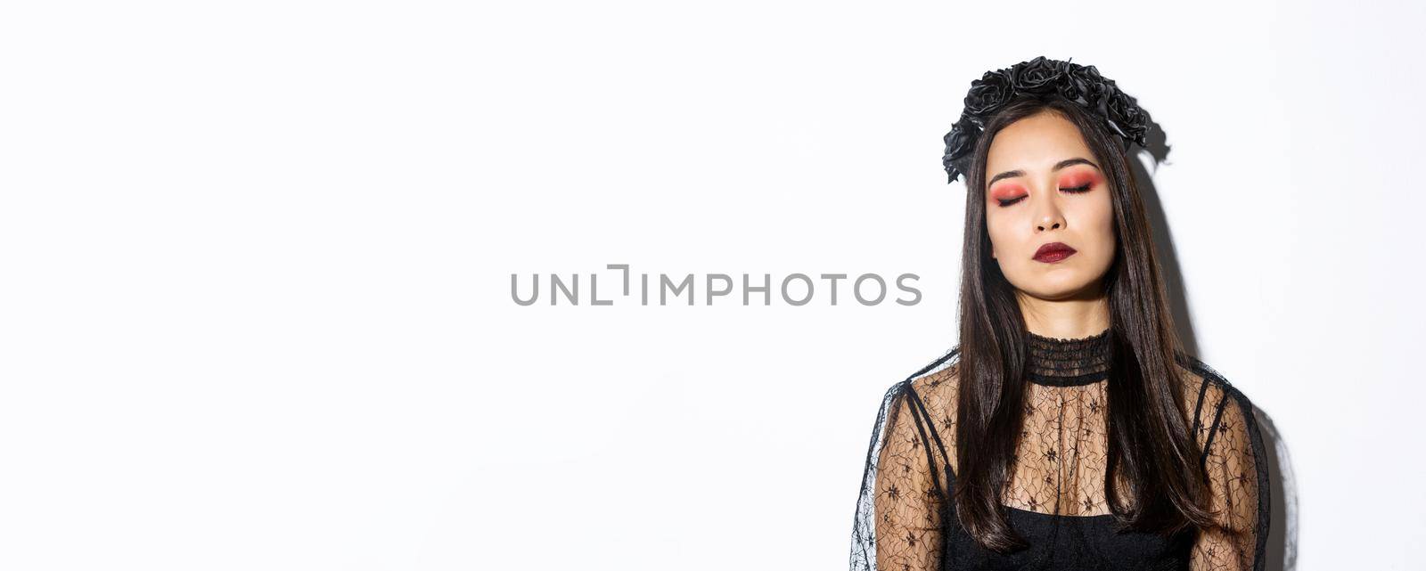 Close-up of bored asian woman sleeping while standing over white background in witch costume.