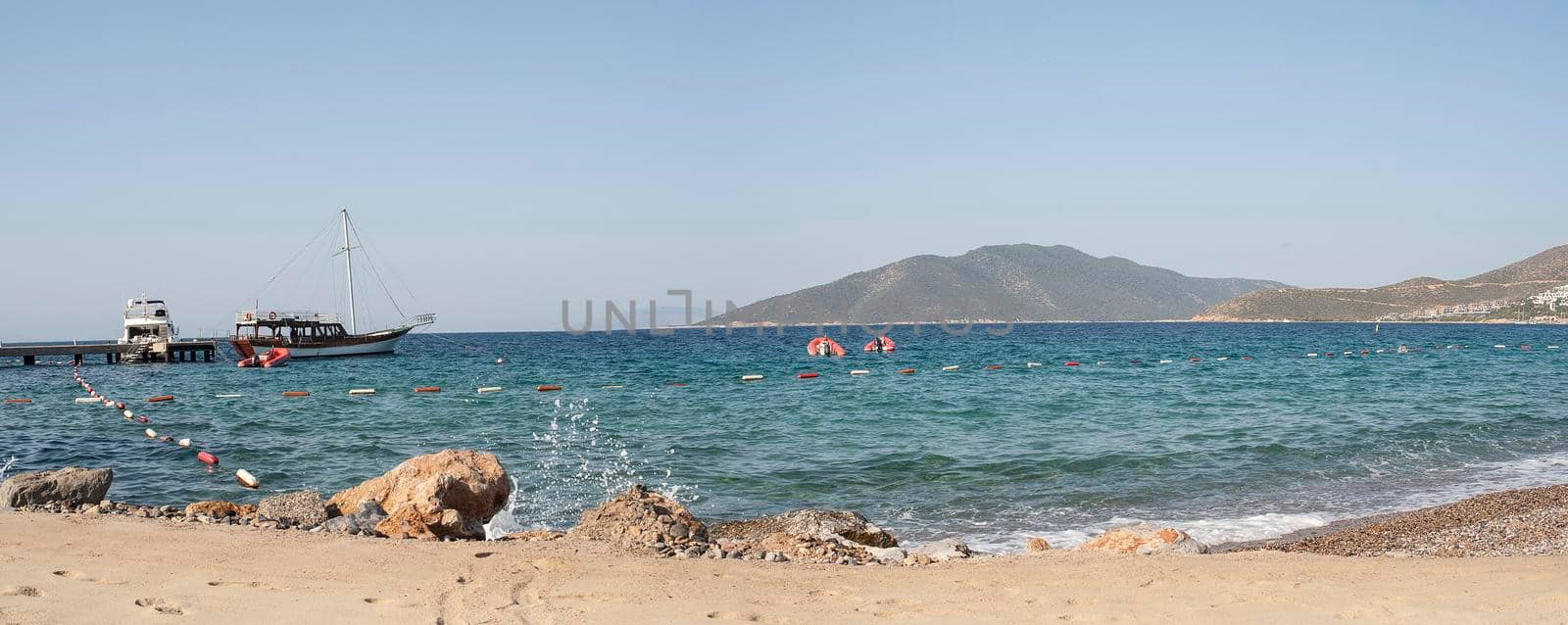 Bodrum - nice view of the sea. Beach Bodrum with sand and mountains, the sea with the ship. Beautiful harbor near the sandy beach.