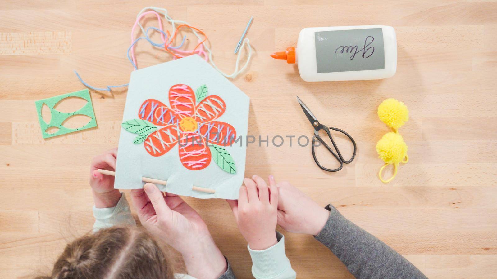 Little girl learning how to sew with her mother at the craft table.