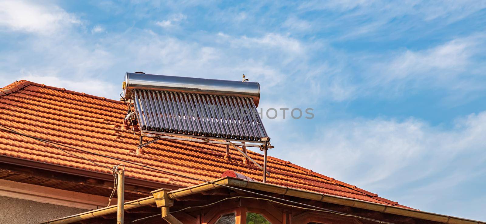 Solar water heater installed on tile roof of house for eco heating of water. Large water tank. Horizontal photo. by EdVal