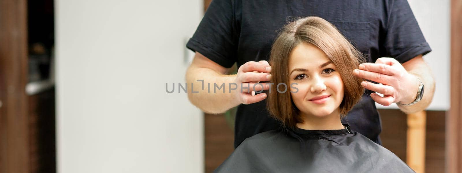 Gorgeous brunette short hair woman and her male hairdresser looking and checking out hairstyle. Beautiful hairstyle of a young brunette woman, results of hair treatment in a beauty salon. by okskukuruza