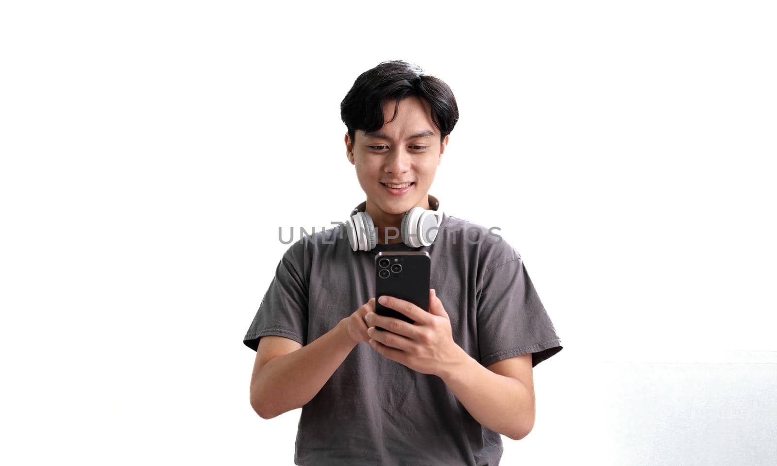 Asian man with headphones listening music using smartphone app while standing over isolated white background.