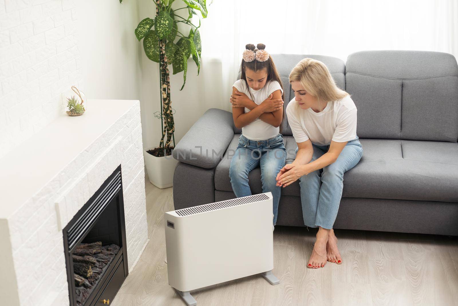 Mother and child warming hands near electric heater at home, closeup