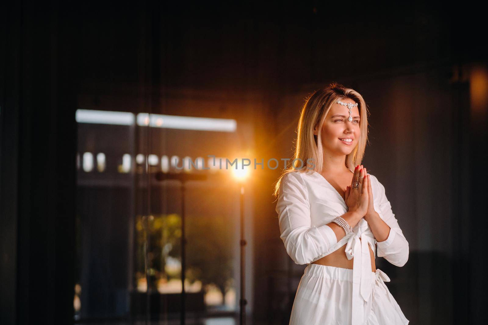 Portrait of a smiling girl in a white dress with her palms clasped in front of her.