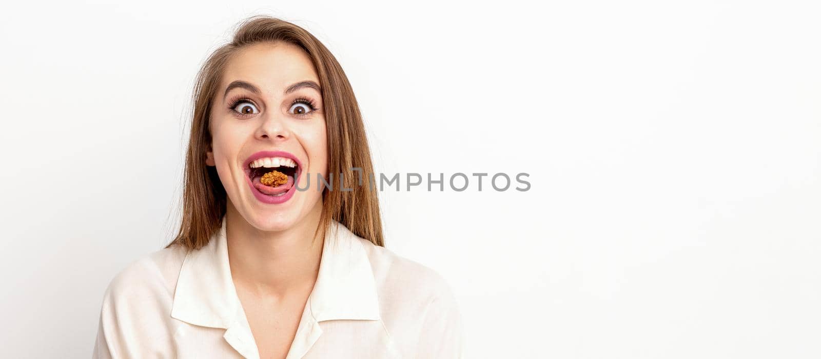 Happy young caucasian woman eating walnuts with an open mouth on white background with copy space