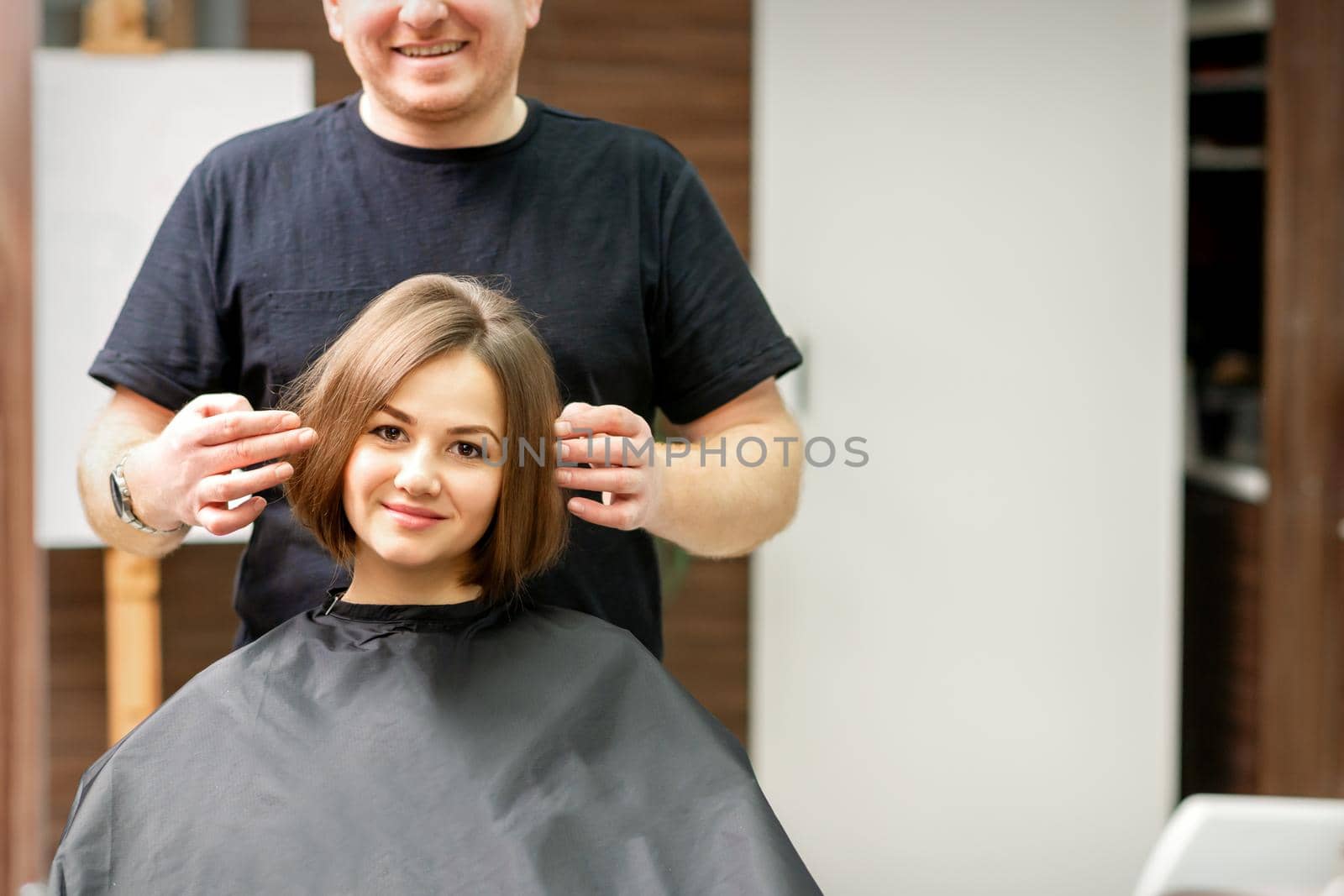 Gorgeous brunette short hair woman and her male hairdresser looking and checking out hairstyle. Beautiful hairstyle of a young brunette woman, results of hair treatment in a beauty salon