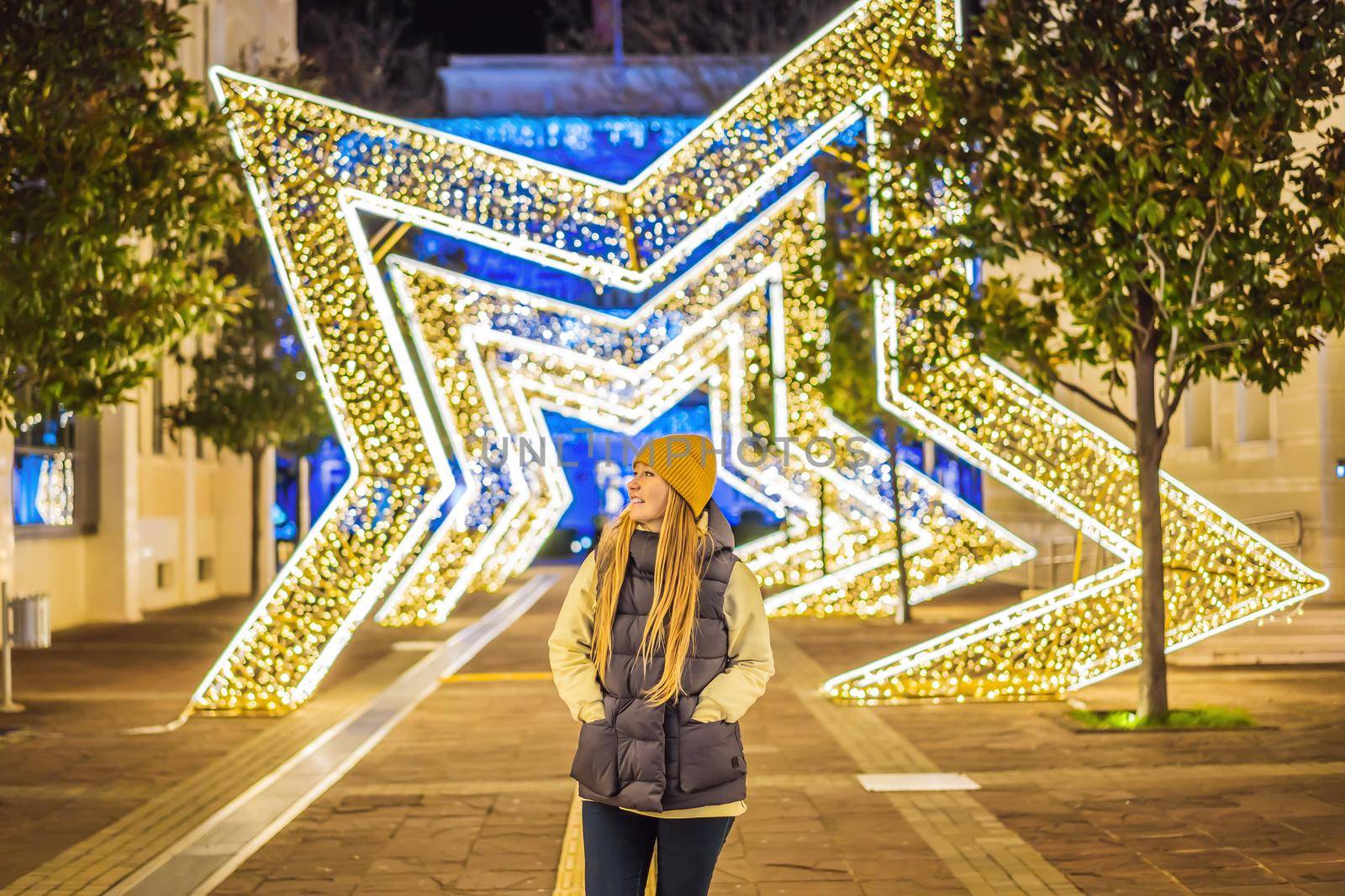 Girl walking in Christmas traditional market decorated with holiday lights in the evening. Winter portrait beautiful young woman outdoors in front of Xmas holidays decorations.