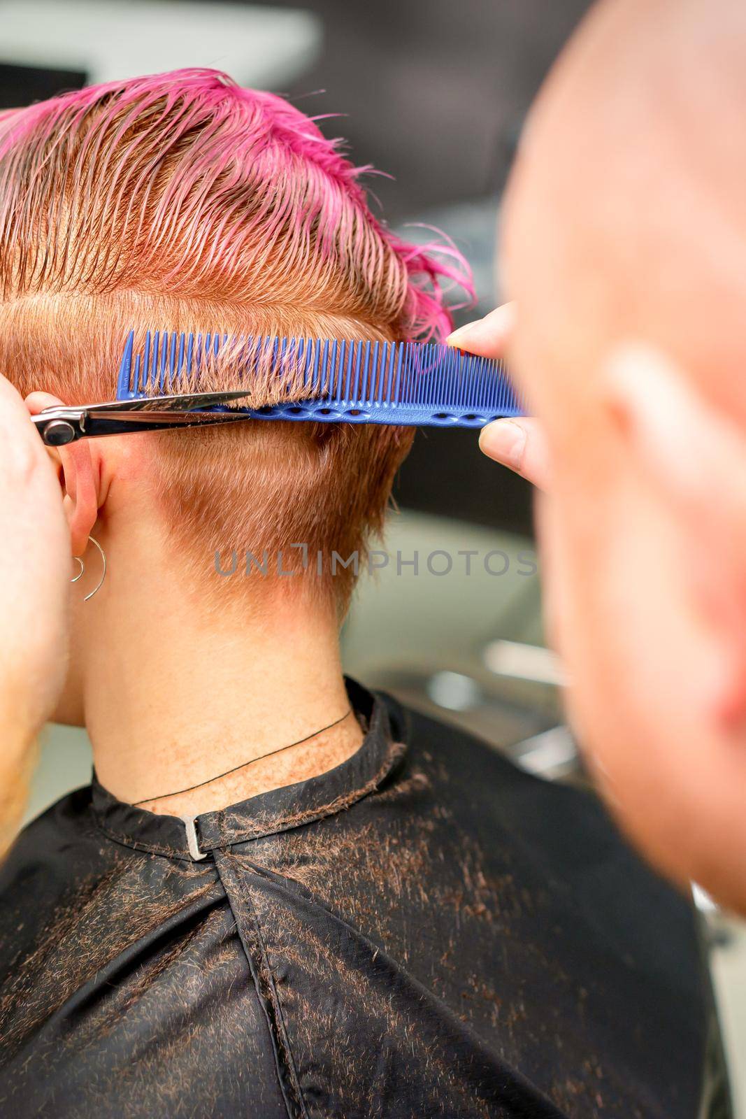 Haircut of dyed short pink wet hair of young caucasian woman by a male hairdresser in a barbershop. by okskukuruza