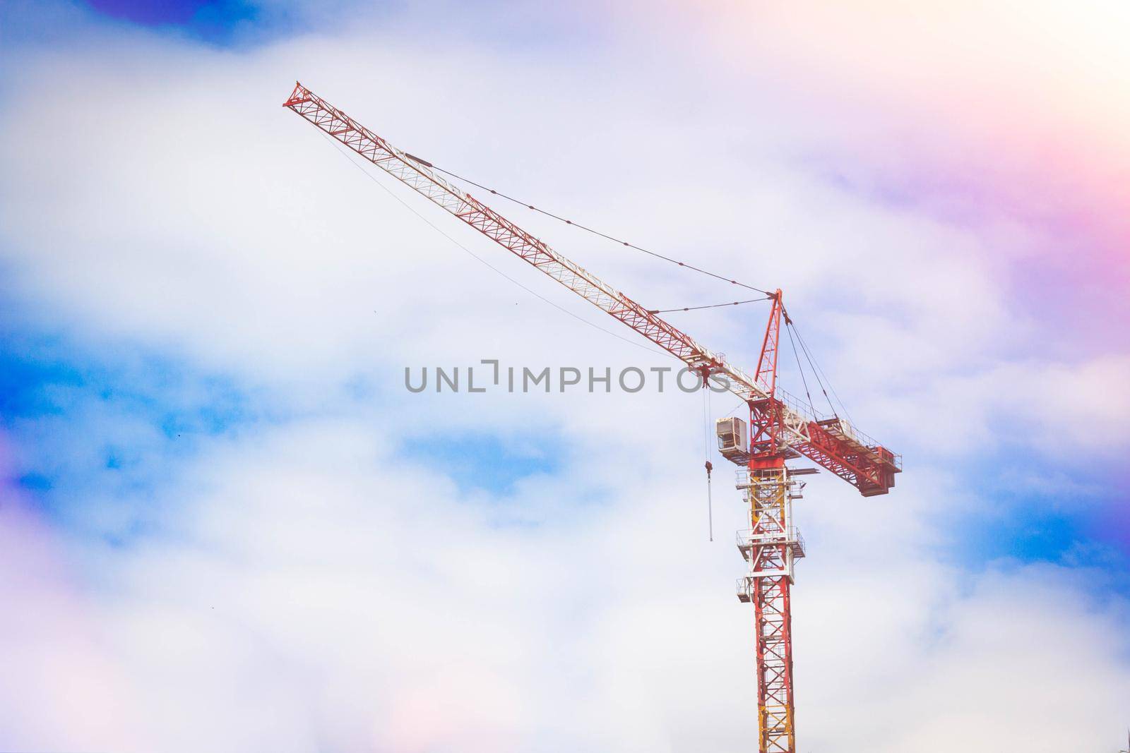 Construction crane in rays of bright sun. House under construction and crane. Construction site. Construction of new house.