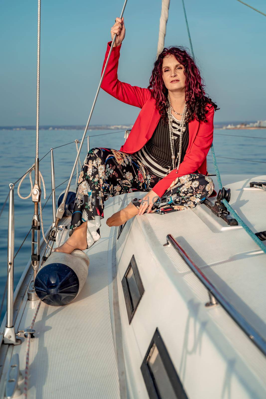 A woman sits on the bow of a yacht on a sunny summer day, the breeze develops her hair, a beautiful sea is in the background.