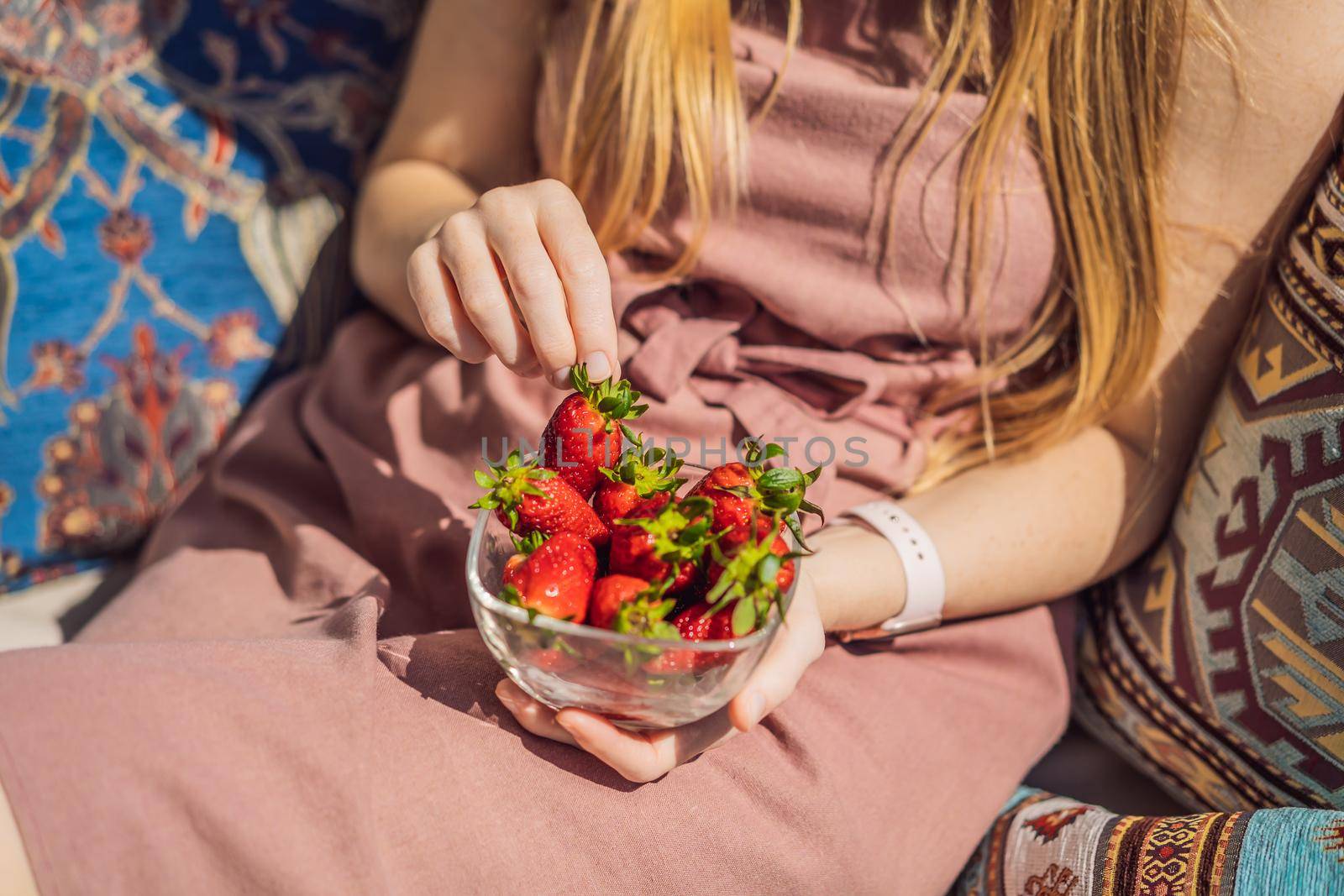 Portrait of gorgeous woman wearing beautiful dress sitting in a patio and eating strawberry.