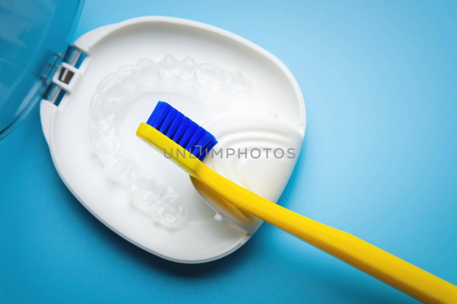 a white special box container for invisible plastic braces, aligners, with a bright yellow toothbrush lie on a blue background. nobody by yanik88