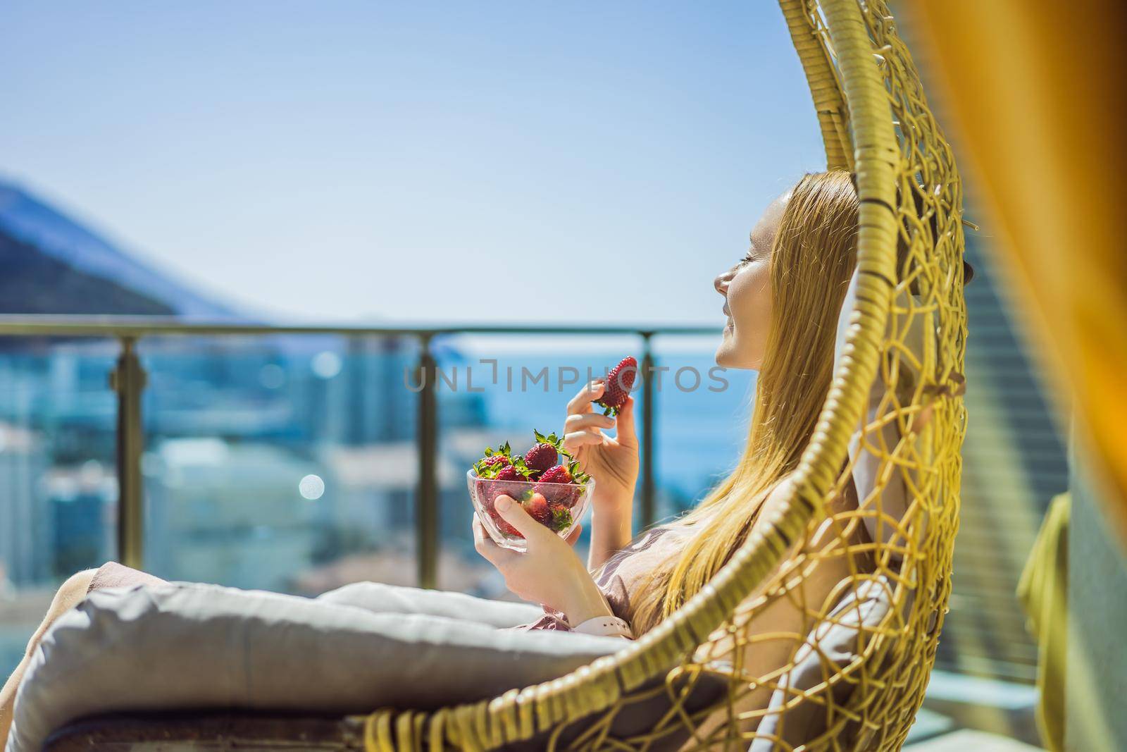 Portrait of gorgeous woman wearing beautiful dress sitting in a patio and eating strawberry.