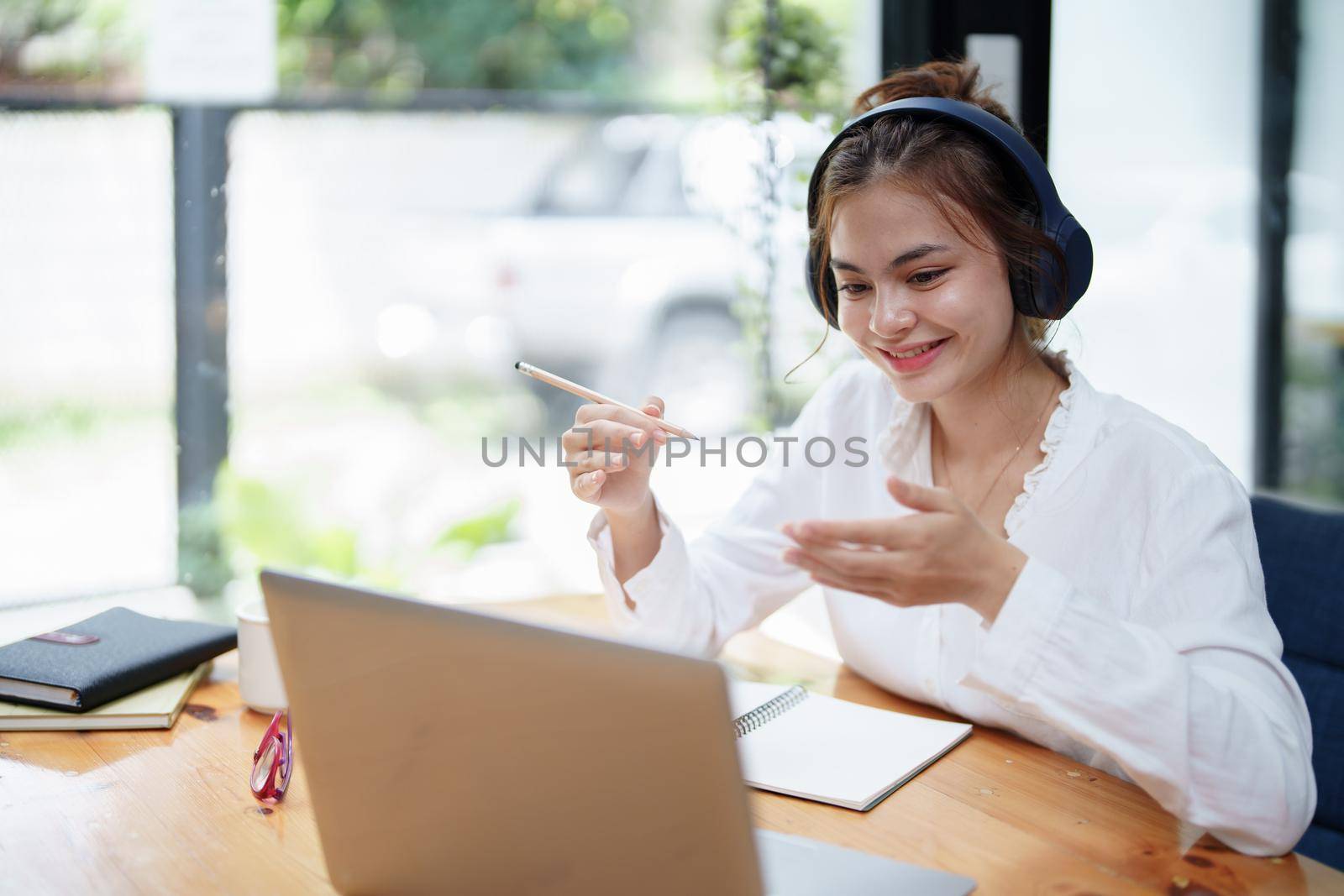 Portrait of a beautiful woman using a computer, earphone and notebook during a video conference