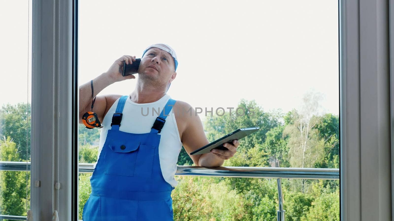 attractive Construction worker is discussing something on the phone, makes measurements of windows, makes notes in tablet. service man , builder examines the object. High quality photo