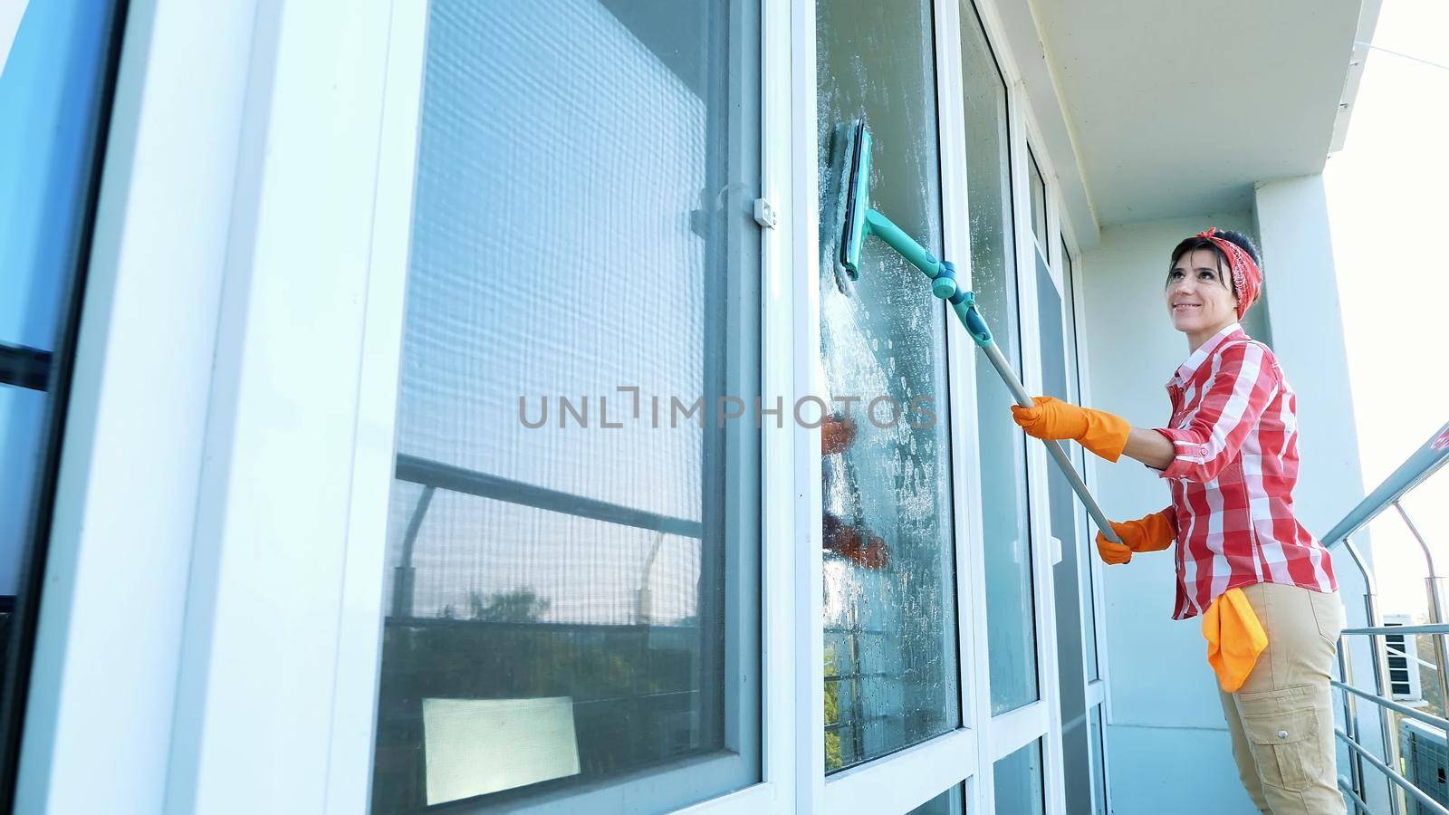 smiling Caucasian Beautiful woman, housewife or Cheerful female worker of cleaning service, in gloves, Cleaning, washing Windows by special mop, enjoying her work. Cleaning lady. High quality photo