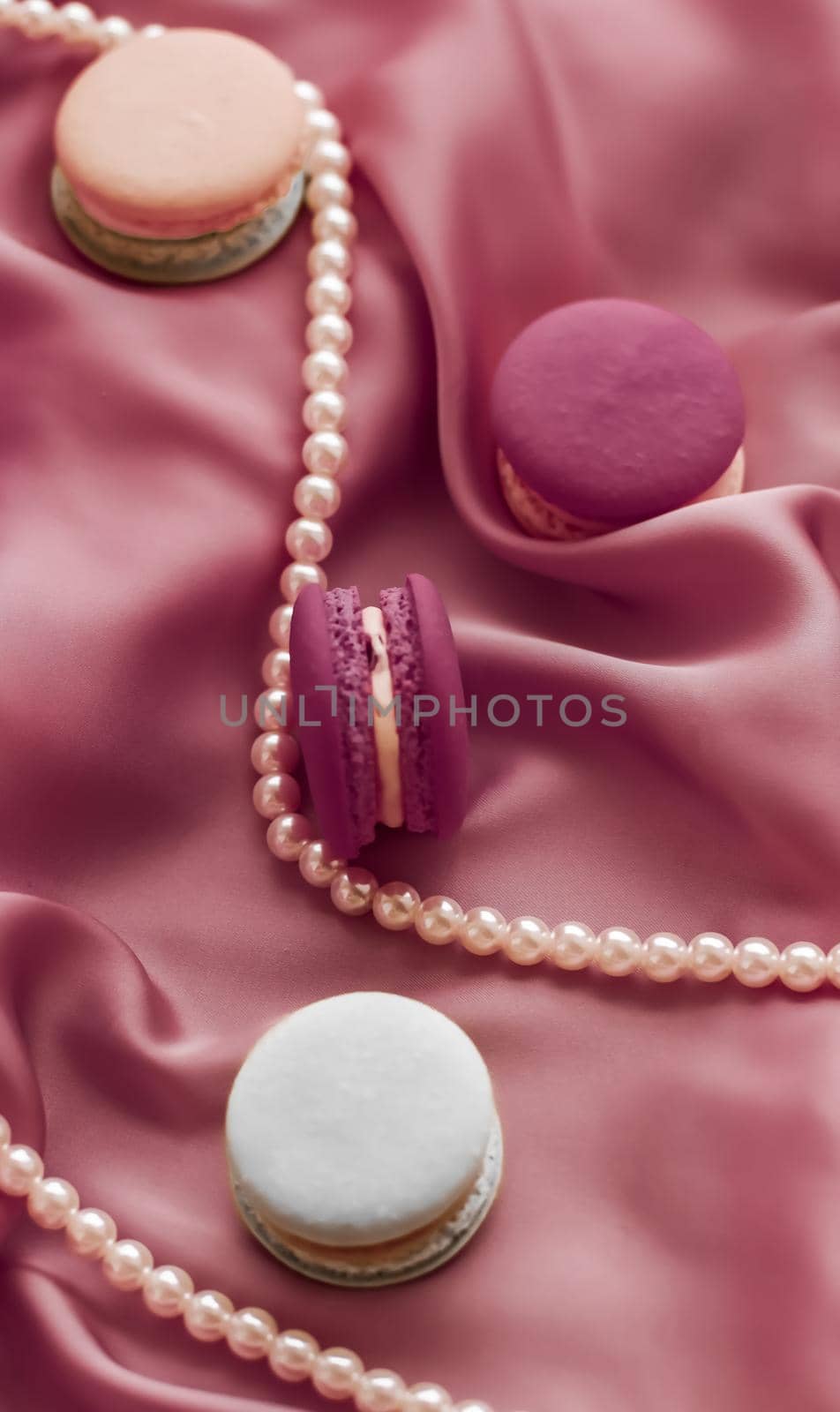 Girly, bakery and branding concept - Sweet macaroons and pearls jewellery on silk background, parisian chic jewelry, French dessert food and cake macaron for luxury confectionery brand, holiday gift