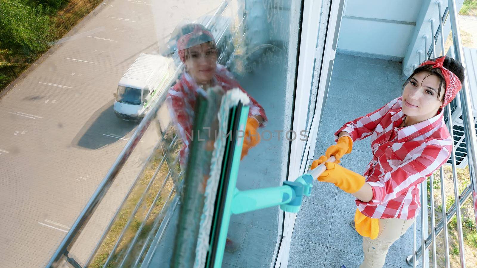 in the window glass is reflected smiling Caucasian Beautiful woman, in gloves, Cleaning, washing Window by special mop, enjoying her work. Cleaning service. High quality photo