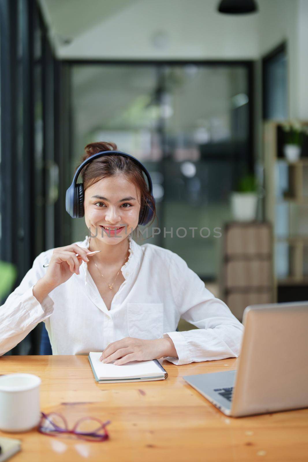 Portrait of a beautiful woman using a computer, earphone and notebook during a video conference