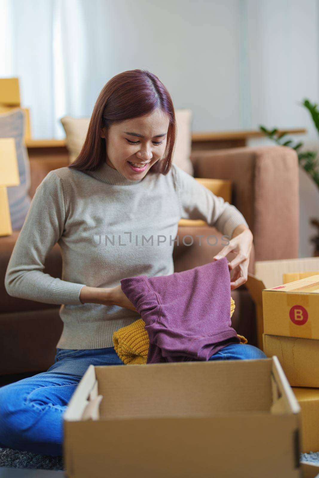 Portrait of a small startup Asian female entrepreneur SME owner picking up shirt before packing it in an inner box with a customer. Online Business Ideas and Freelance.