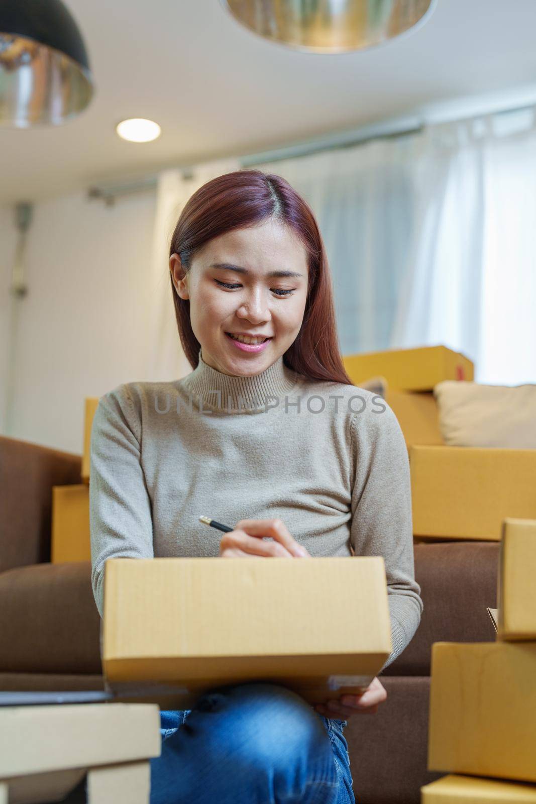 A portrait of a small startup, an SME owner, an Asian female entrepreneur checking orders to arrange the produce before packing the products in the inner boxes with the customers. Freelance concepts by Manastrong