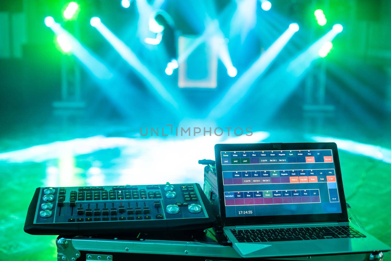 Highlighted deejay mixing with laptop on the stage with blue beams and lightshow.