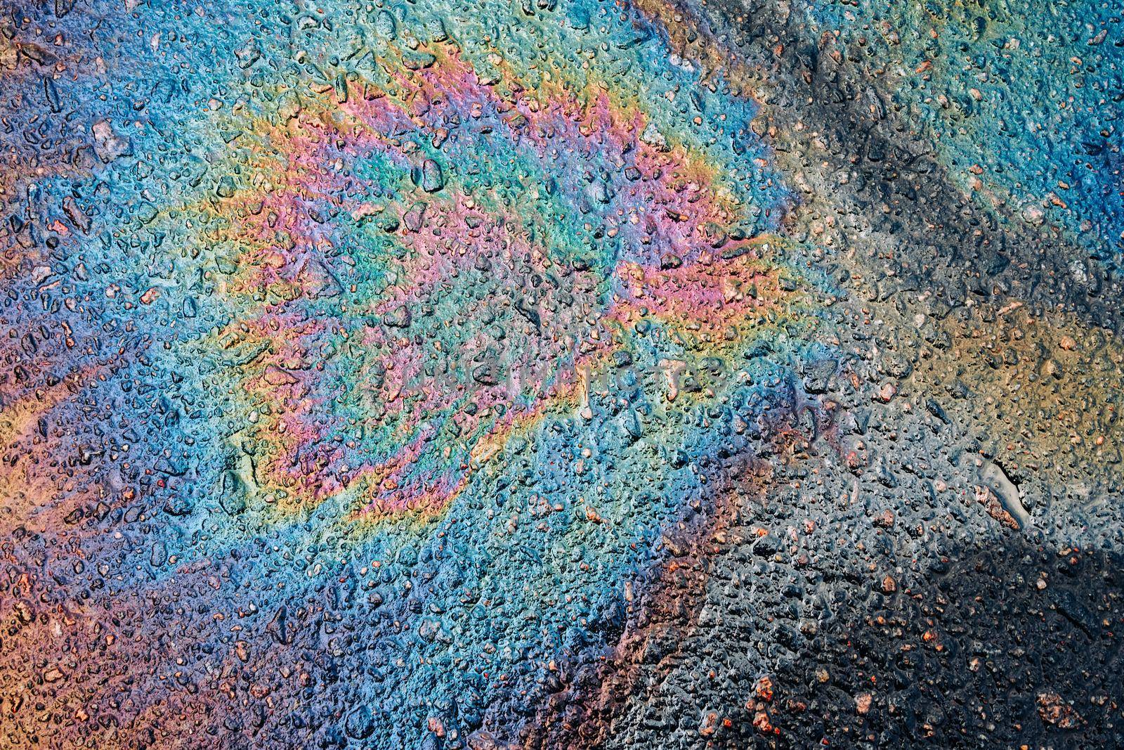 A beautiful colored shiny spot of oil, gasoline or diesel fuel on the wet asphalt. Leaked petroleum products on the roadway.