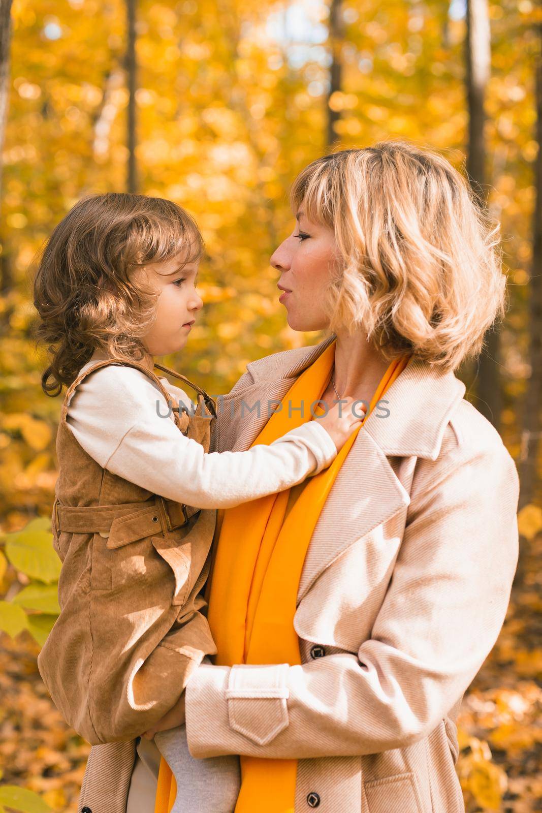 Woman with kid girl outdoors in fall. Child kissing mom. Mothers day holiday and autumn concept